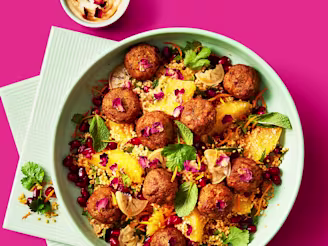 Moroccan falafels served on top of vegetarian couscous topped with pomegranate seeds in a blue bowl and a sauce on the side