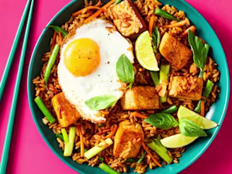 Nasi Goreng on a plate with golden tofu, a fried egg, lime wedges, Thai basil, and chopsticks on the side.