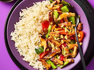 Oyster sauce stir fry served in a purple bowl with white rice, chopped vegetables and a fork with a side of nuts to garnish.