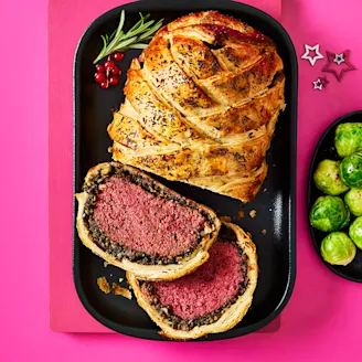 Tofu wellington cut in a serving dish with a side of Brussel sprouts on a pink background.