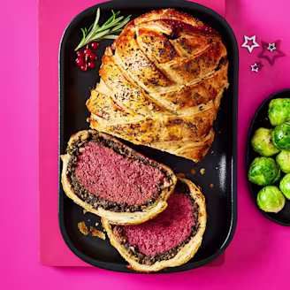 Tofu wellington cut in a serving dish with a side of Brussel sprouts on a pink background.