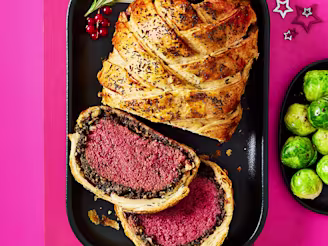 Tofu wellington cut in a serving dish with a side of Brussel sprouts on a pink background.