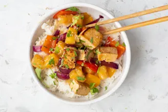 Sweet and sour tofu in bowl with white rice and chopsticks.