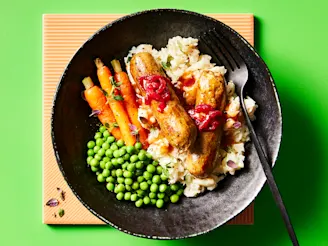 Cauldron Lincolnshire sausages served on a bed of mashed potato with roasted carrots and peas on the side, served in a dark dish