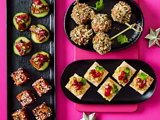 Assortment of vegan christmas canapes on black serving plates on a bright pink background.