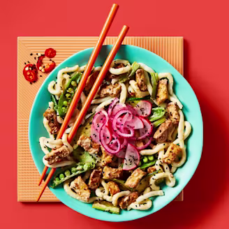 Vegan satay stir fry with udon noodles showcasing Cauldron Tofu and a vegetable served on a blue bowl with orange chopsticks 