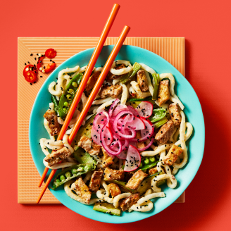 Vegan satay stir fry with udon noodles showcasing Cauldron Tofu and a vegetable served on a blue bowl with orange chopsticks 