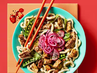 Vegan satay stir fry with udon noodles showcasing Cauldron Tofu and a vegetable served on a blue bowl with orange chopsticks