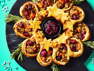 Puff pastry wreath made up of pastry cups and cut out stars assembled on a black serving board on a teal background.