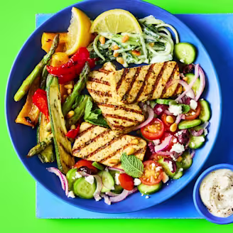 Greek Tofu Bowl served on a plate with grilled tofu, Greek salad, chargrilled vegetables, and tzatziki on the side.