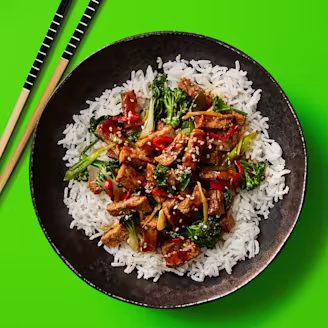 Wok Fried Cauldron Hoisin Tofu served on a bed of white rice served in a dark dish with chopsticks on the side