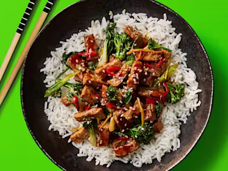 Wok Fried Cauldron Hoisin Tofu served on a bed of white rice served in a dark dish with chopsticks on the side