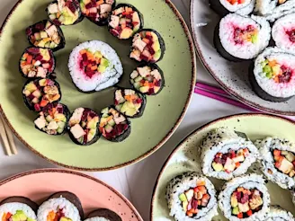 Four plates of vegan sushi rolls with Cauldron marinated tofu pieces filled with seaweed, carrot, cucumber, avocado, pepper, beetroot and sesame seeds.