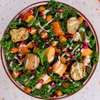Kale and pumpkin salad with a tahini dressing in an orange rimmed bowl with Caudlron Middle Eastern Falafels in blue packaging.