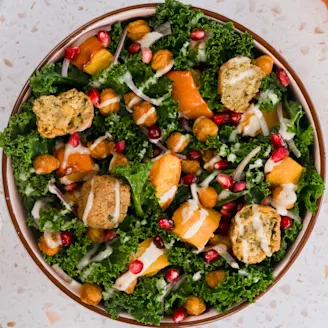 Kale and pumpkin salad with a tahini dressing in an orange rimmed bowl with Caudlron Middle Eastern Falafels in blue packaging.