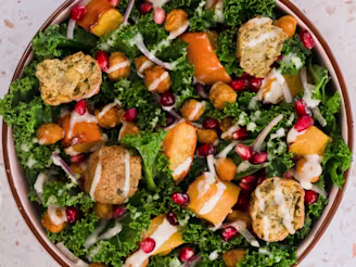Kale and pumpkin salad with a tahini dressing in an orange rimmed bowl with Caudlron Middle Eastern Falafels in blue packaging.