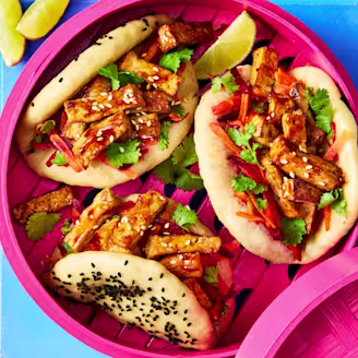 Teriyaki Tofu Bao Buns topped with coriander and sesame seeds, served with lime wedges on a pink dish.