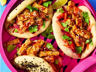 Teriyaki Tofu Bao Buns topped with coriander and sesame seeds, served with lime wedges on a pink dish.