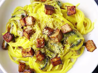 Yellow carbonara spaghetti pasta with tofu in deep white bowls, small dish with parmesan cheese to side.