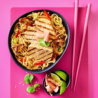 Yaki soba noodles with slices of Cauldron Extra Firm Tofu served in a dark dish with pink chopstick 
