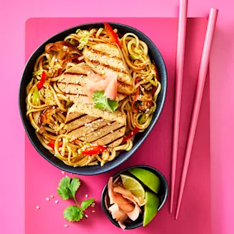 Yaki soba noodles with slices of Cauldron Extra Firm Tofu served in a dark dish with pink chopstick 