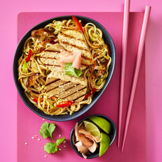 Yaki soba noodles with slices of Cauldron Extra Firm Tofu served in a dark dish with pink chopstick 