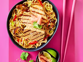 Yaki soba noodles with slices of Cauldron Extra Firm Tofu served in a dark dish with pink chopstick