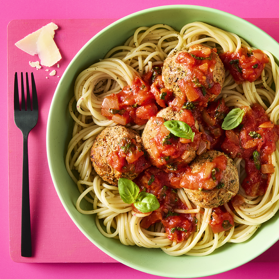 Tofu Meatballs & Pasta with parmesan and basil leaves in a green bowl on a pink background.