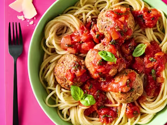Tofu Meatballs & Pasta with parmesan and basil leaves in a green bowl on a pink background.