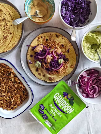 Shredded Cauldron Authentic Tofu in a dish with open tortilla, red cabbage, red onion, chipotle mayonnaise and green Cauldron Tofu packaging.