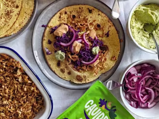 Shredded Cauldron Authentic Tofu in a dish with open tortilla, red cabbage, red onion, chipotle mayonnaise and green Cauldron Tofu packaging.