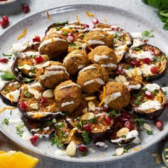 Aubergine and falafel bake loaded with tahini, pomegranate & flaked almonds on a plate