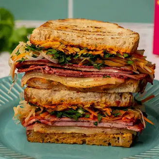 Rainbow vegetable and miso soaked beetroot Cauldron Extra Firm Tofu layered in sourdough bread on a blue plate.
