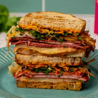 Rainbow vegetable and miso soaked beetroot Cauldron Extra Firm Tofu layered in sourdough bread on a blue plate.
