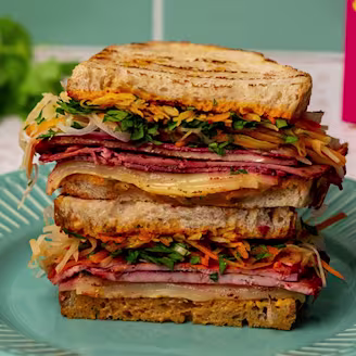 Rainbow vegetable and miso soaked beetroot Cauldron Extra Firm Tofu layered in sourdough bread on a blue plate.