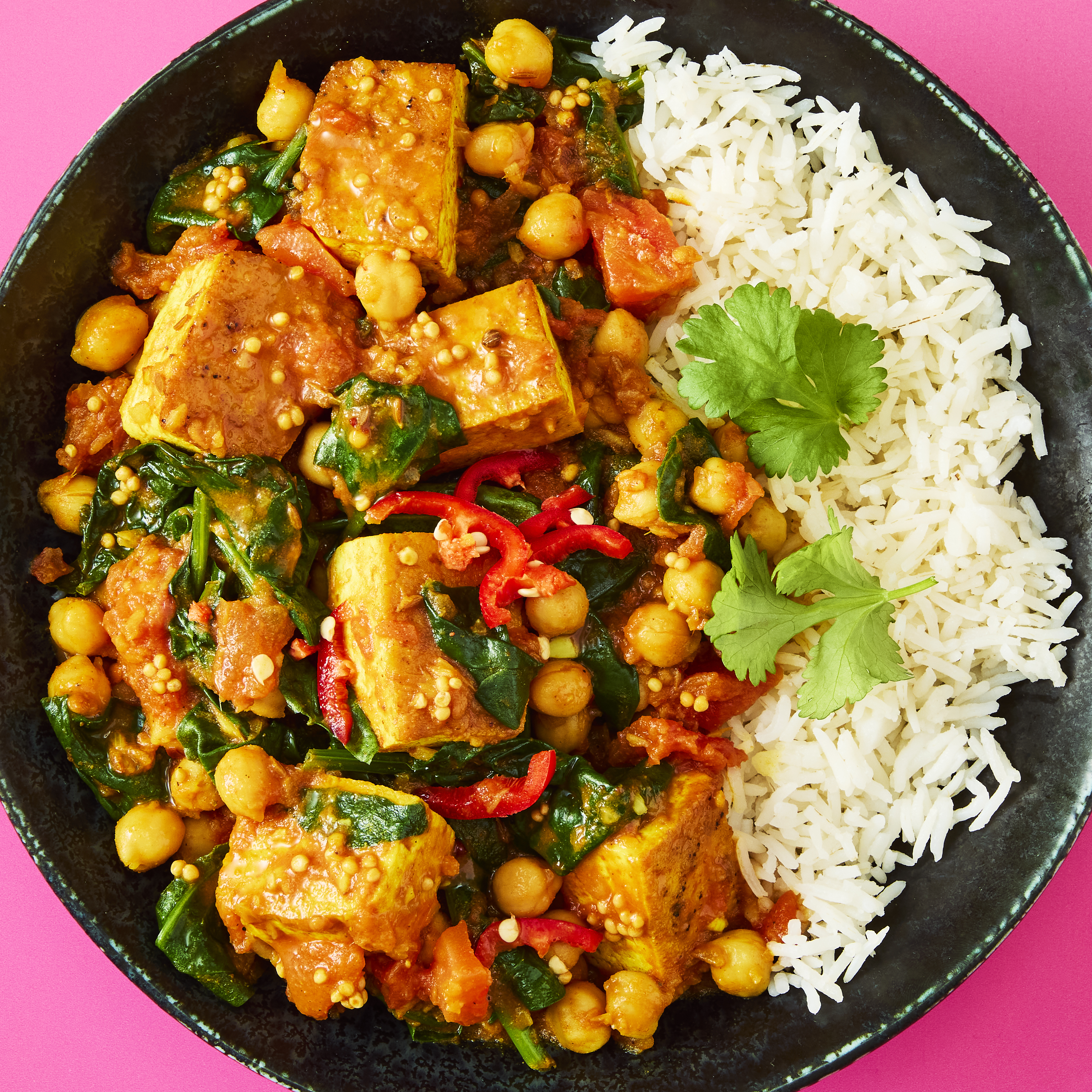 Tofu, Spinach & Chickpea Curry with white rice served on a black plate.