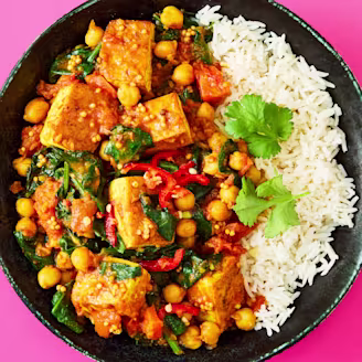 Tofu, Spinach & Chickpea Curry with white rice served on a black plate.