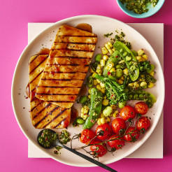 Two Tofu Steaks served alongside vegetables including green peans and tomatoes served on a white plate with a pink background 
