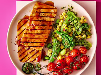Two Tofu Steaks served alongside vegetables including green peans and tomatoes served on a white plate with a pink background