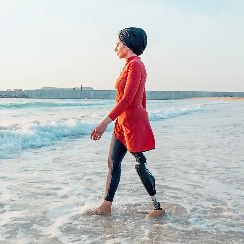 Zainab Al Eqabi trägt eine Prothese an ihrem linken Bein und spaziert damit am Strand entlang.