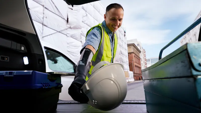 Man reaches for his helmet in the trunk with his michelangelo prosthetic hand.