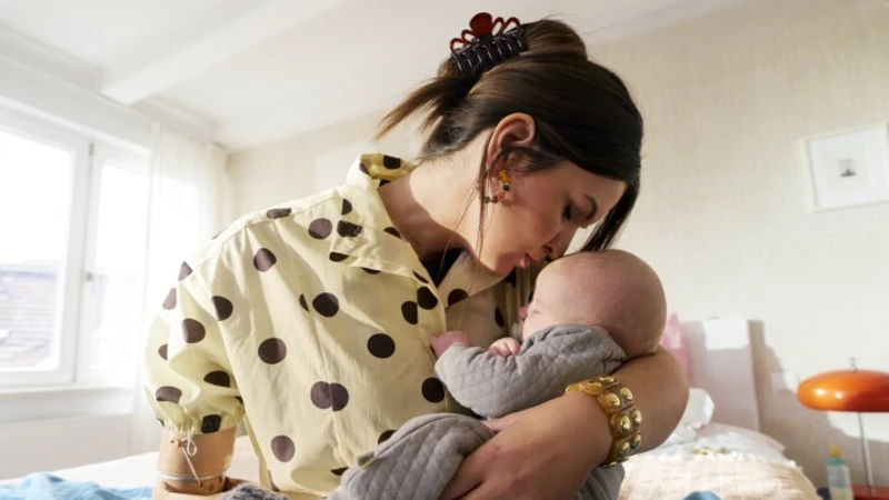 Mother with Michelangelo prosthetic hand gently holding her baby while sitting on a bed in a bright home environment