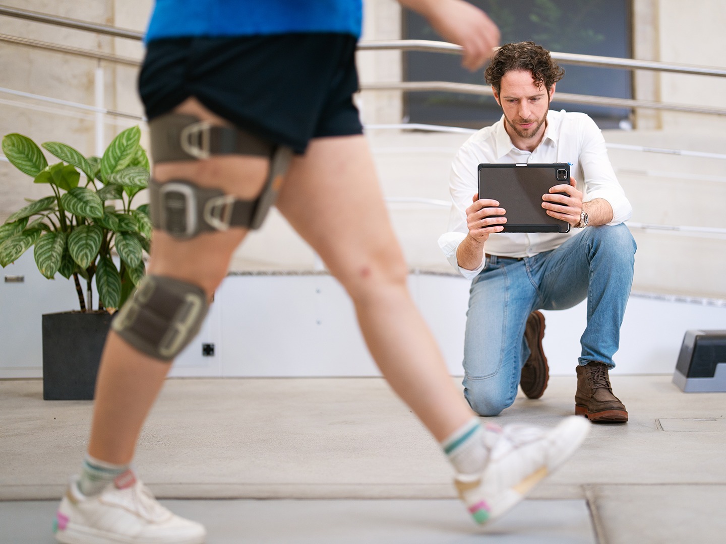Clinician using a tablet to analyze walking pattern during fitting of an orthotic knee brace in a rehabilitation clinic
