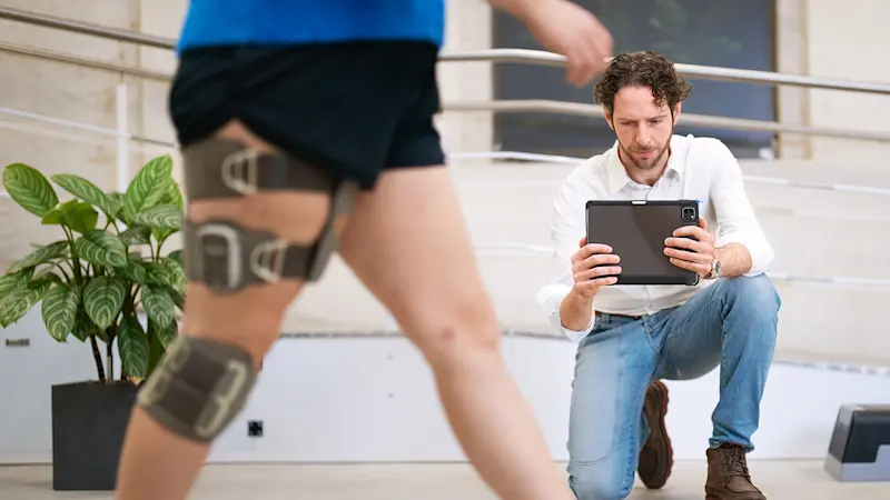 Clinician using a tablet to analyze walking pattern during fitting of an orthotic knee brace in a rehabilitation clinic