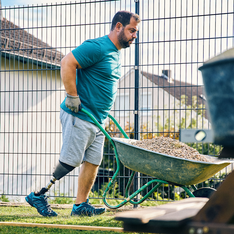 MyFit TT Anwender Beytullah Demir arbeitet in seinem Garten und schiebt eine Schubkarre umher.