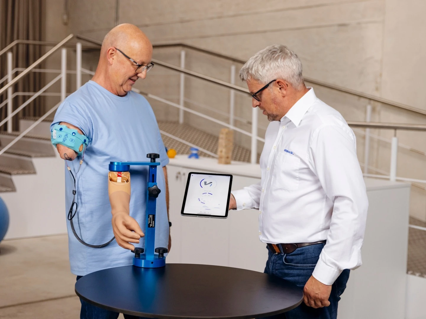 Man with upper arm prosthesis during modern prosthetic fitting, technician explaining digital analysis on a tablet in a rehabilitation center