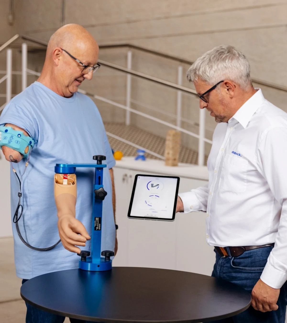 Man with upper arm prosthesis during modern prosthetic fitting, technician explaining digital analysis on a tablet in a rehabilitation center