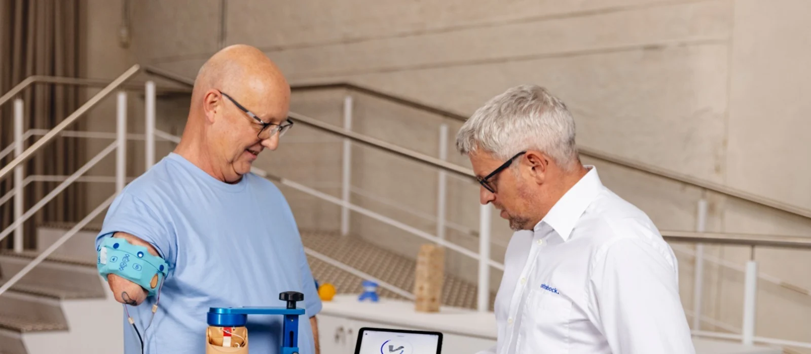 Man with upper arm prosthesis during modern prosthetic fitting, technician explaining digital analysis on a tablet in a rehabilitation center