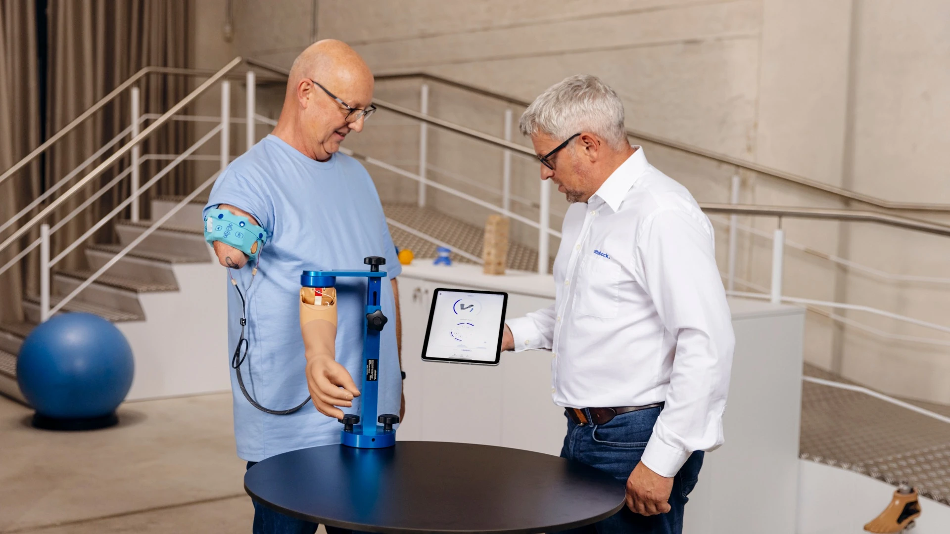 Man with upper arm prosthesis during modern prosthetic fitting, technician explaining digital analysis on a tablet in a rehabilitation center