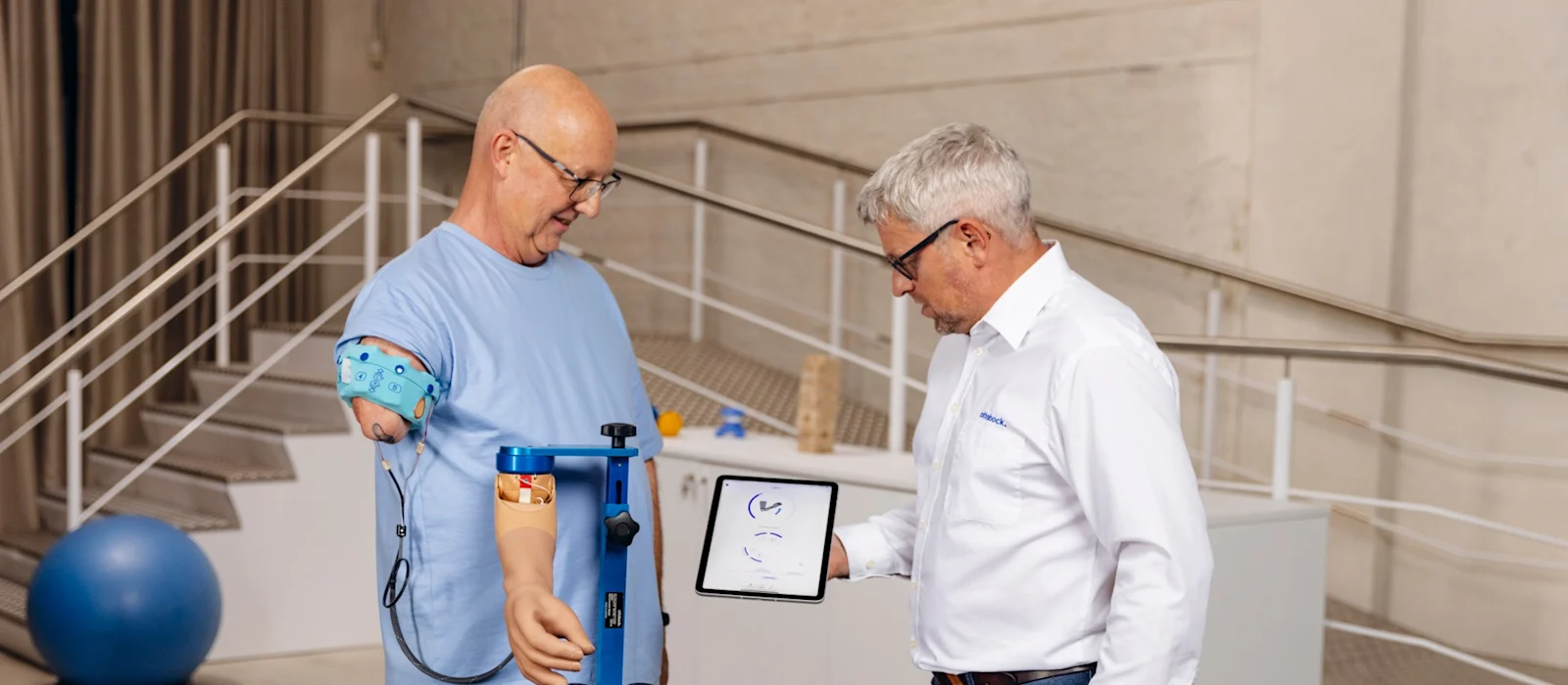 Man with upper arm prosthesis during modern prosthetic fitting, technician explaining digital analysis on a tablet in a rehabilitation center